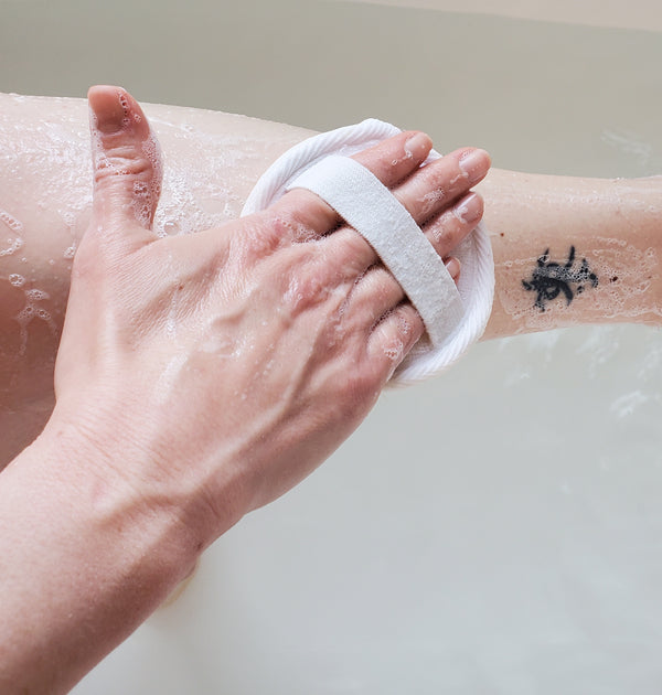 A photo of a luffa pad in use. The pad is held in a hand, with the elastic band around the hand. The luffa pad is being rubbed against skin.