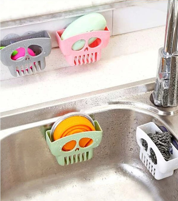 A photo of four colors of skull soap saver baskets suctioned in or near a sink. Each one is a different color, and each holds a different item, either soap, a toy, a steel scrubber, or lids.