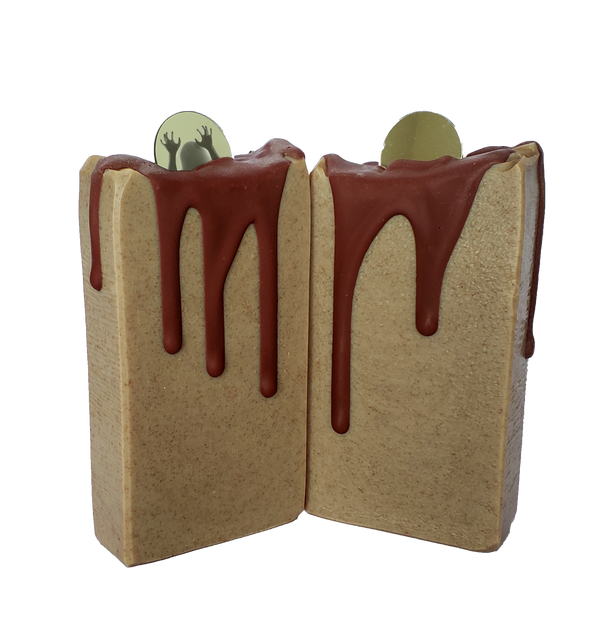 Two bars of Bloody Mary soap. The soap bars are tan with red drips running down them. A small round mirror sits on top. The mirror on the left soap bar shows a shadowy figure reaching up.