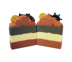 Two bars of Pirate Queen soap. Each bar is layered, with dark orange at the bottom, creamy white in the middle, and dark brown on top. The bars feature a dark orange piped top with small soaps in the shape of gold doubloons and either a coppery pistol or a dark brown ship wheel.