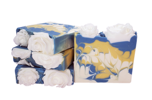 Four bars of Rose soap. The bars contain blue, yellow, and white swirls and are topped with white soap roses.