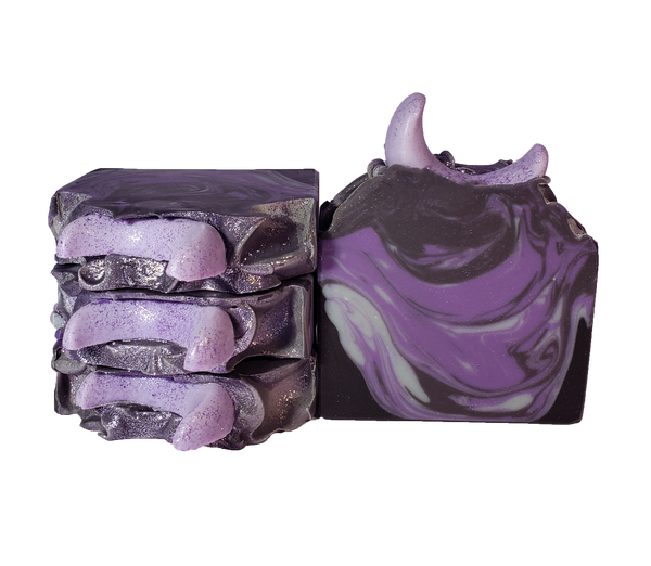 Four bars of The Moon soap. Each bar contains purple, gray, and black swirls and is topped with a light purple crescent moon and purple glitter.