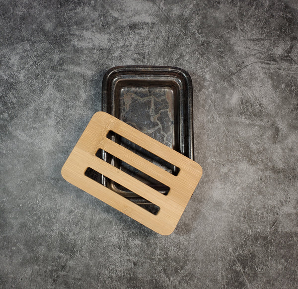 A dark brown, rectangular ceramic soap dish accompanied by a bamboo slotted tray. The background is gray.