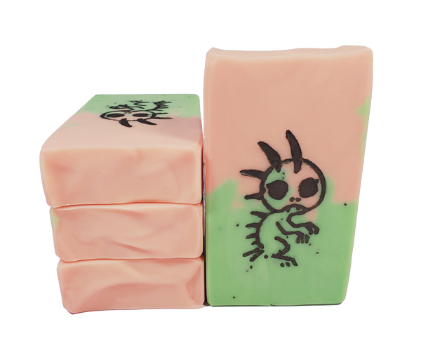 Four bars of Chupacabra soap, which are peach and lime colored with poppy seeds. A lizard-like creature is stamped on the bar.