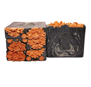 Four bars of Death soap. The bars are black with gray swirls, with a sugar skull stamped onto the bar face. The soaps are topped with orange soap flowers and glitter.