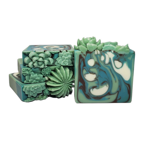Four bars of Hegemone soap. The bars contain swirls of green, white, and brown and are topped with a variety of green soap succulents.
