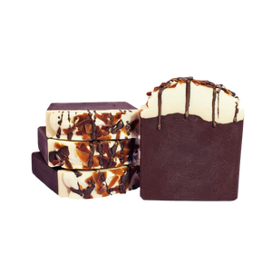 Four bars of Monkey Bomber soap. The bars are dark brown with flecks of coffee grounds evenly dispersed throughout the bars. The bars are white on top, with brown soap shavings and brown soap drizzle to mimic chocolate.